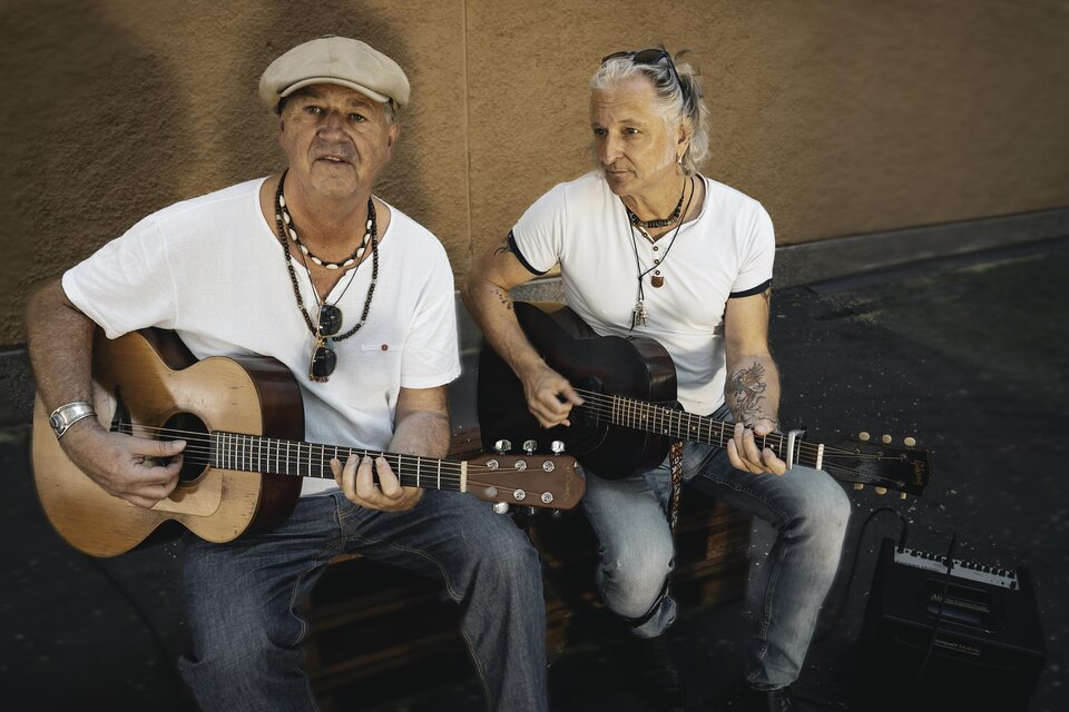 Zwei Musiker sitzen auf einer Kiste und spielen Akustikgitarre. Sie tragen lockere Kleidung und haben eine entspannte Ausstrahlung. | © Violeta Lenz