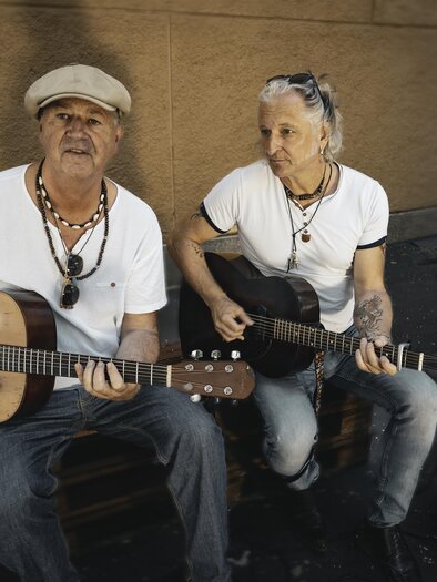Two musicians are sitting on a box and playing acoustic guitar. They are wearing loose clothing and have a relaxed demeanor. | © Violeta Lenz