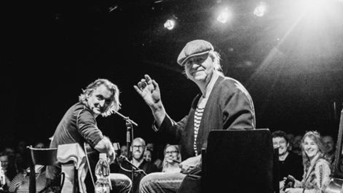 Zwei Musiker sitzen auf einer Bühne und interagieren mit dem Publikum. Die Atmosphäre ist entspannt und freundlich. | © Lupi Spuma