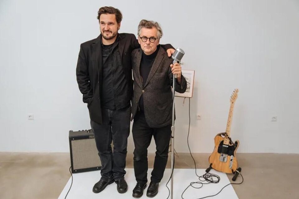 Zwei Männer stehen nebeneinander und lächeln. Im Hintergrund sind ein Mikrofon, ein Gitarrenverstärker und eine Gitarre zu sehen. | ©  David Višnjić