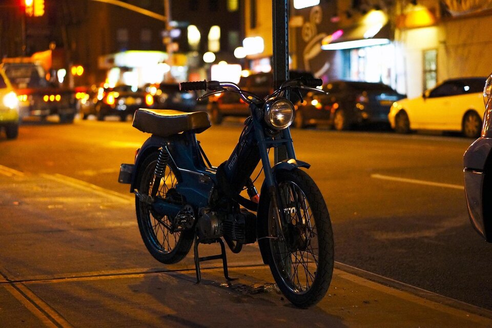Ein blaues Moped steht auf der Straße bei Nacht. Im Hintergrund sind Autos und Straßenlichter sichtbar. | © Pixabay