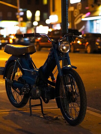 A blue moped is parked on the street at night. In the background, cars and streetlights are visible. | © Pixabay
