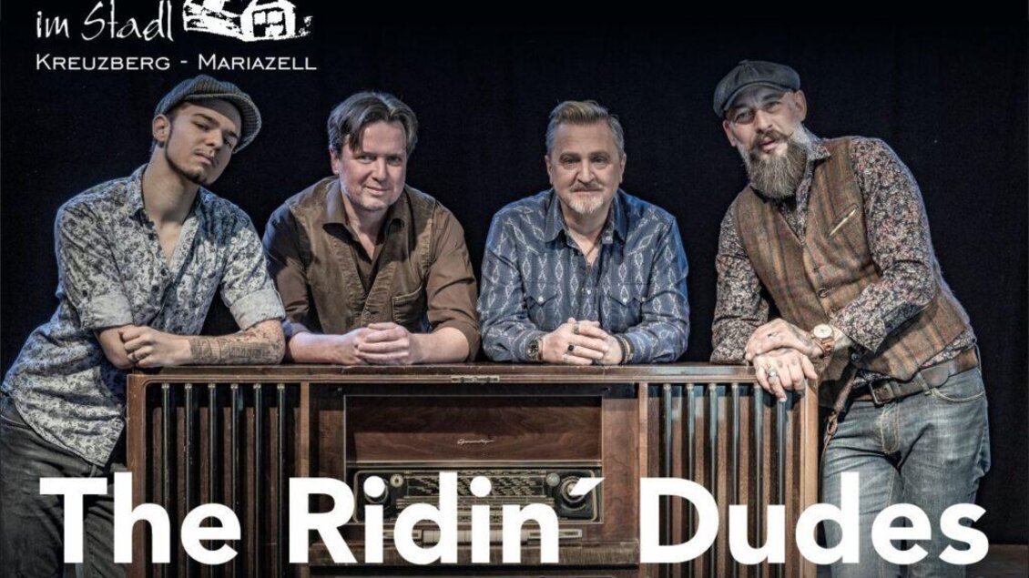 Eine Gruppe von vier Männern steht zusammen und lächelt. Im Hintergrund sind zwei Scheinwerfer zu sehen, die den Fokus auf die Gruppe lenken. | © Ridin' Dudes