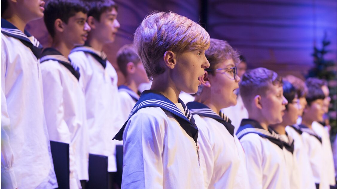 Eine Gruppe von Jungen in Matrosenanzügen singt in einem Chor. Die Szenerie ist festlich und die Jungen zeigen konzentrierte Gesichtsausdrücke. | © Lukas Beck