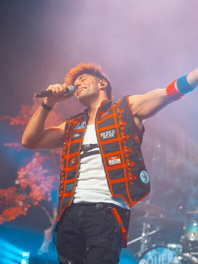 Alexander Eder sings with a microphone on a well-lit stage in Seiersberg-Pirka, with a drummer in the background. | © Alexander Eder
