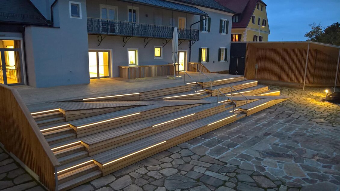 Eine moderne Holztreppe mit LED-Beleuchtung führt zu einem Gebäude. Die Atmosphäre ist abends ruhig und einladend. | © Stieglerhaus