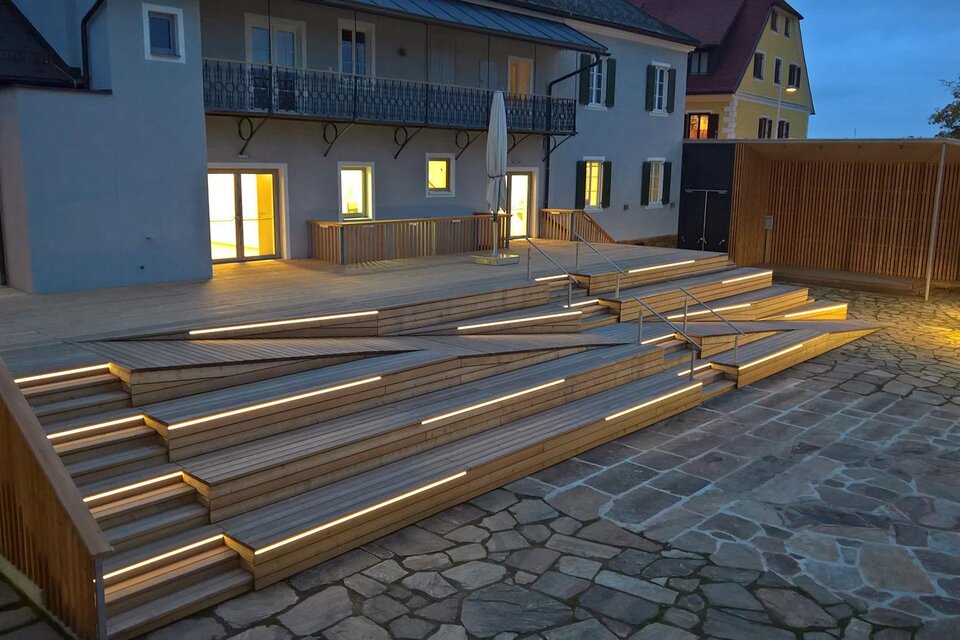 Eine moderne Holztreppe mit LED-Beleuchtung führt zu einem Gebäude. Die Atmosphäre ist abends ruhig und einladend. | © Stieglerhaus