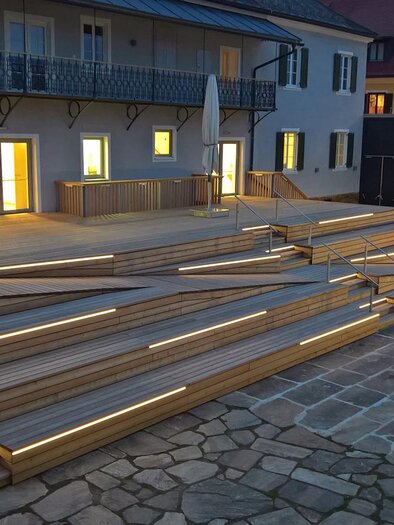 Eine moderne Holztreppe mit LED-Beleuchtung führt zu einem Gebäude. Die Atmosphäre ist abends ruhig und einladend. | © Stieglerhaus