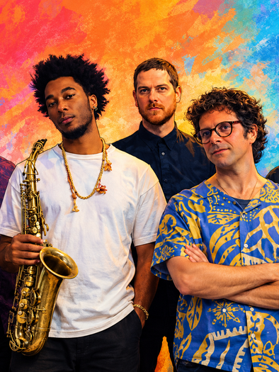 Five musicians from the Brazilian All-Star Quintet, one of them with a saxophone, in front of a colorful background. | © ChatGPT-Christine Rotschädl