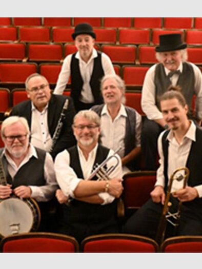 A group of eight musicians in historical outfits sits in a theater with red seats. They are holding instruments and smiling at the camera. | © Daniil Bobrov
