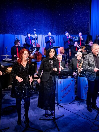 A lively music performance with several singers and a large band in the background. The artists are elegantly dressed and radiate energy. | © Petru Rimovetz