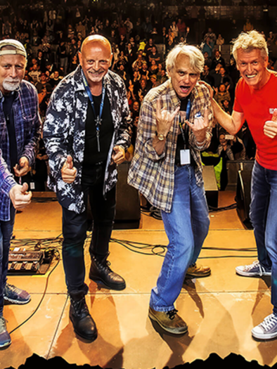 A band is on stage and is happily posing for the audience. In the background, many fans can be seen enjoying the performance. | © Manfred Feichtinger