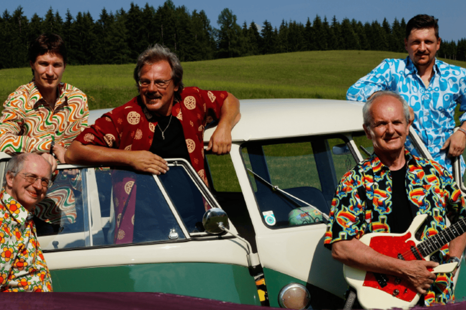 Eine Gruppe von fünf Musikern steht vor einem klassischen VW-Bus. Sie tragen bunte Hemden und lächeln in die Kamera. | © Gemeinde Gamlitz