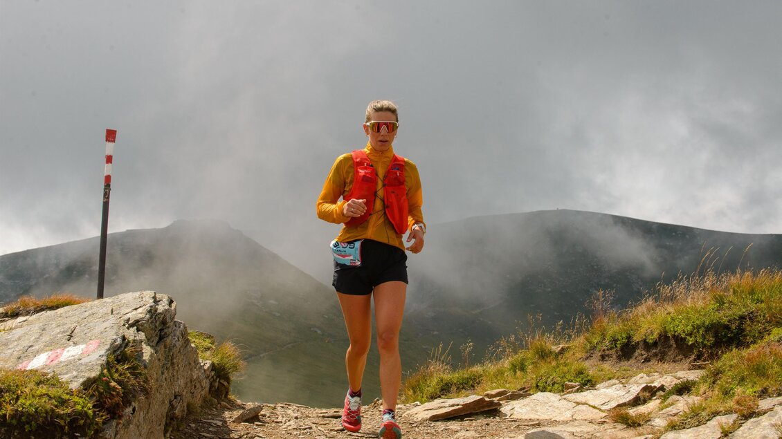 Eine Person joggt auf einem steinigen Pfad in den Bergen. Der Himmel ist bewölkt und die Landschaft ist steinig und grün. | © Christian Prattes