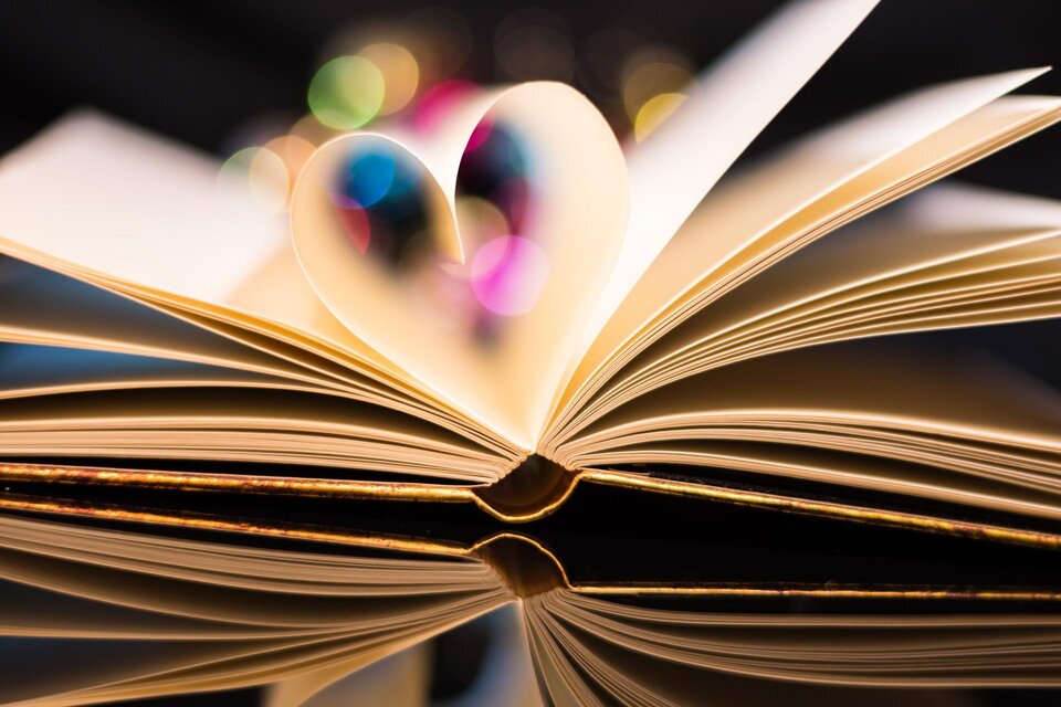 Ein aufgeschlagenes Buch mit Seiten, die die Form eines Herzens bilden. Bunte Lichter im Hintergrund verleihen der Szene eine romantische Atmosphäre. | © pixabay
