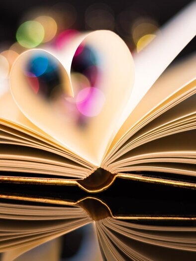 Ein aufgeschlagenes Buch mit Seiten, die die Form eines Herzens bilden. Bunte Lichter im Hintergrund verleihen der Szene eine romantische Atmosphäre. | © pixabay