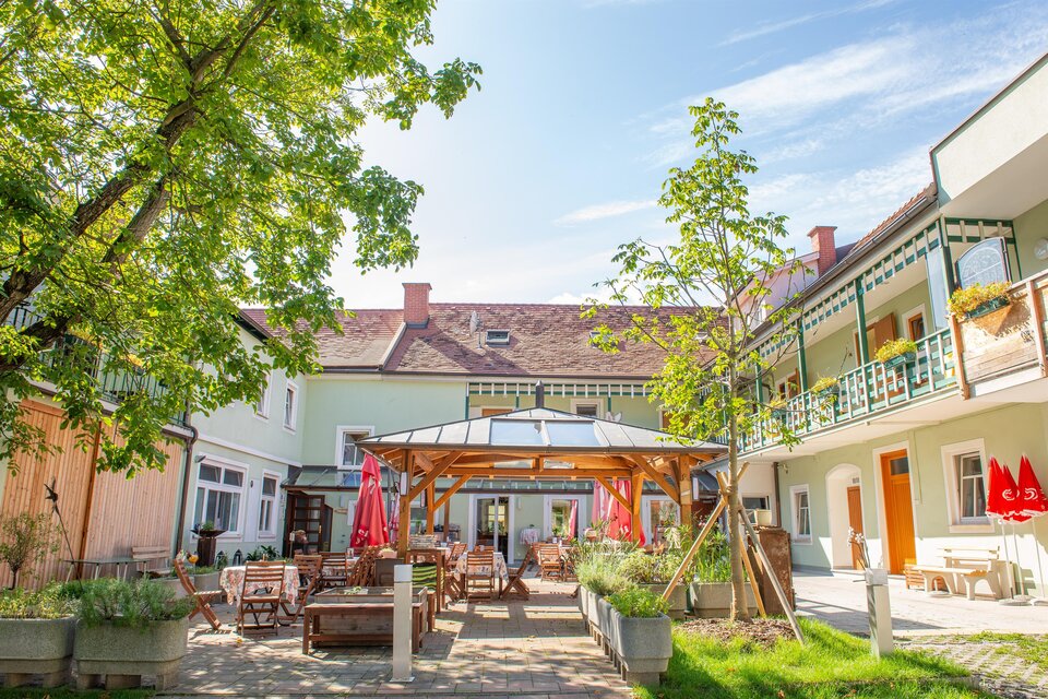 Ein freundlicher Innenhof mit Sitzgelegenheiten und grünen Pflanzen. Im Hintergrund sind helle Gebäude und ein blauer Himmel sichtbar. | © H. Schweighofer