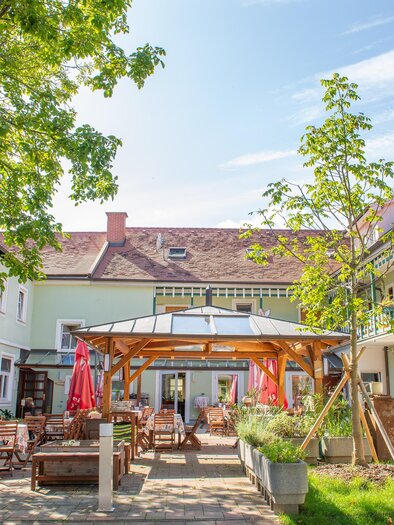 Ein freundlicher Innenhof mit Sitzgelegenheiten und grünen Pflanzen. Im Hintergrund sind helle Gebäude und ein blauer Himmel sichtbar. | © H. Schweighofer