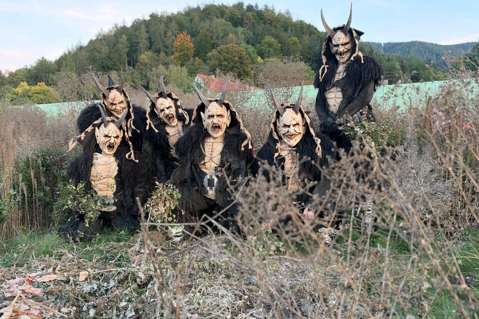 Eine Gruppe von Kreaturen in unheimlichen Kostümen mit Hörnern steht im hohen Gras. Im Hintergrund sind sanfte Hügel und Bäume zu sehen. | © Mühltaler Teifl