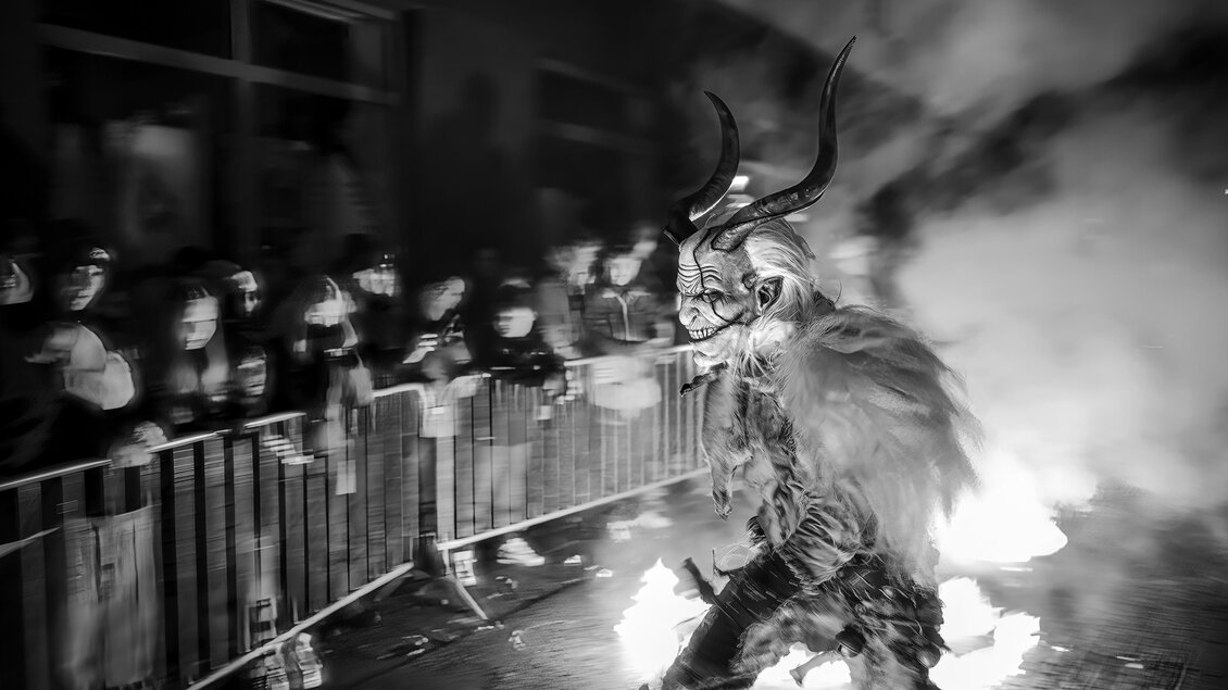 Krampus bei einem Lauf hinter Absperrgitter in einer Rauchwolke, Bild ist schwarz-weiß | © Fabian Anderle