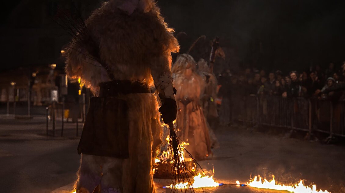 Eine festliche Veranstaltung mit Menschen in traditionellen Kostümen. Im Vordergrund steht eine Person mit einem Hornhelm, umgeben von brennenden Flammen. | © Stadtgemeinde Bärnbach