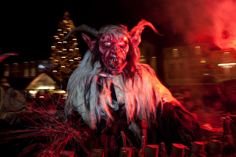 Krampus mit Hörnern, langen Haaren und furchterregender Maske, rot beleuchtet beim nächtlichen Krampuslauf in Voitsberg. | © Graz Tourismus-Harry Schiffer