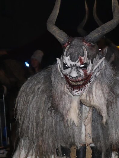 Ein schauriger Charakter mit Hörnern und furchterregendem Gesichtsausdruck. Die Figur trägt einen grauen Pelzmantel und befindet sich in einer Menschenmenge bei Nacht. | © Stoarbruch Teifl| Krampuslauf