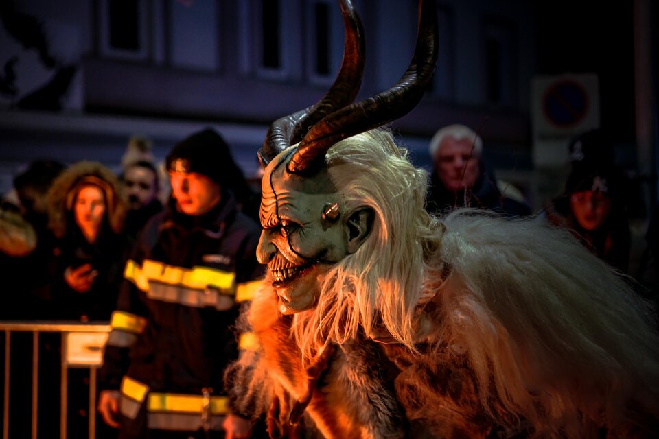 Krampus mit weißen Fell, daneben eine Ordnungsperson am Absperrgitter.  | © Fabian Anderle