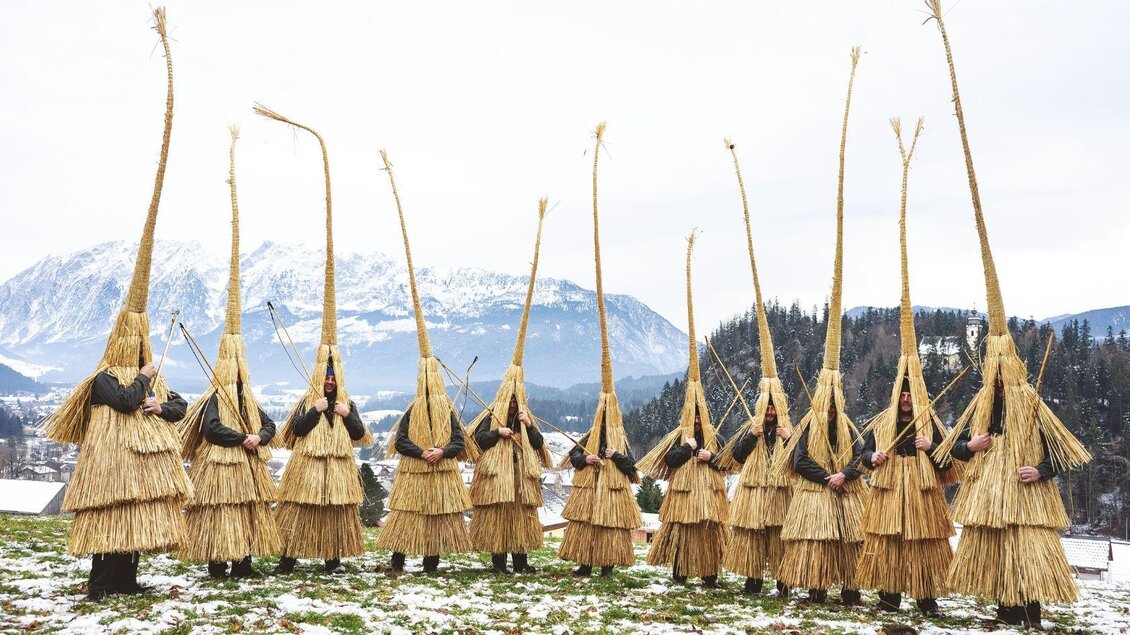 <p>Ein Gruppenfoto der Schab in ihren traditionellen Strohgewand. Im Hintergrund ist der verschneite Grimming zu sehen.</p> | © Lebensbilder - Christine Struz
