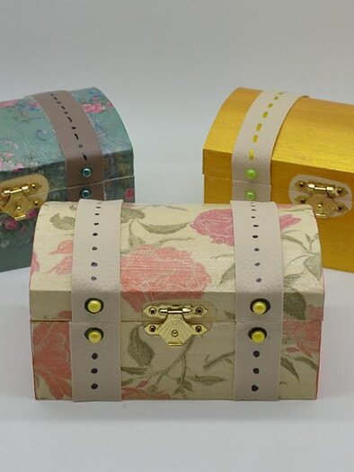 Three decorative treasure chests in different colors stand side by side. Each chest has a unique design with colorful patterns and a clasp. | ©  MuseumsCenter