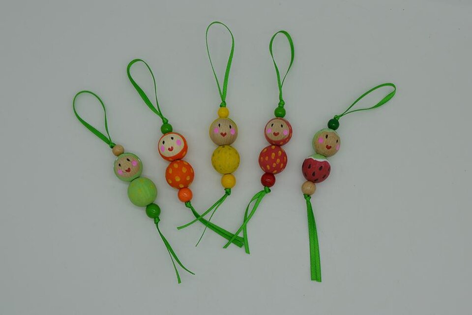 Bunte Holzanhänger in Form von kleinen Figuren mit freundlichen Gesichtern. Sie sind mit grünen Bändern zum Aufhängen versehen. | ©  MuseumsCenter Leoben