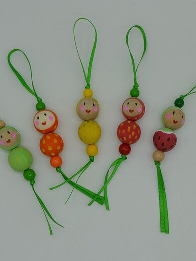 Bunte Holzanhänger in Form von kleinen Figuren mit freundlichen Gesichtern. Sie sind mit grünen Bändern zum Aufhängen versehen. | ©  MuseumsCenter Leoben