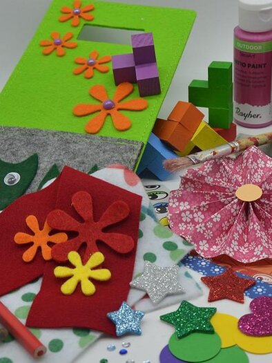 Colorful crafting materials on a table. There are color cards, glitter stars, brushes, and various paper shapes visible. | © KulturQuartier Leoben