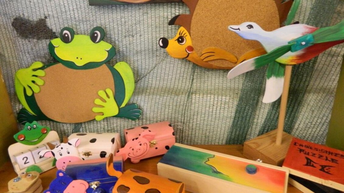 Bunte Bastelarbeiten von Tieren sind auf einem Tisch verteilt. Im Vordergrund sind ein Frosch, ein Schwein und ein gepunkteter Kasten zu sehen.