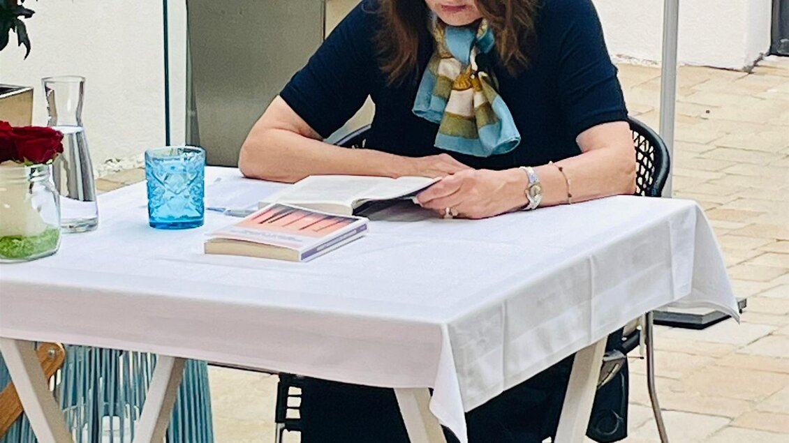 Eine Person sitzt an einem Tisch und liest ein Buch. Im Hintergrund sind Pflanzen und ein paar dekorative Elemente zu sehen. | © © Das Altstadthaus