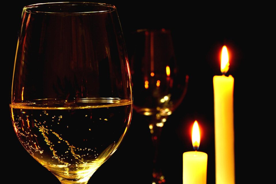 Ein Glas mit einem klaren Getränk steht vor flackernden Kerzen auf schwarzem Hintergrund. Die Szene strahlt eine romantische und gemütliche Atmosphäre aus. | © Pixabay