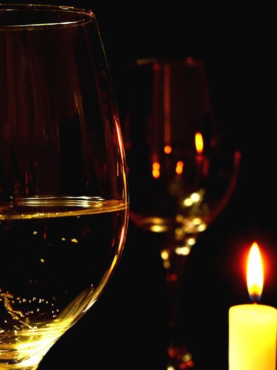 A glass with a clear drink stands in front of flickering candles on a black background. The scene radiates a romantic and cozy atmosphere. | © Pixabay
