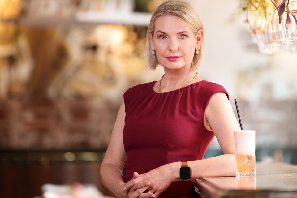 Claudia Rossbacher posiert bei einer Kommode mit einem Getränk daneben, Lesung im Römerhof Eggersdorf. | © Lucija Novak