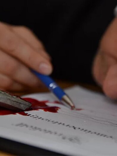 A person is lying on a document with a pen in hand and a bloodstain on the paper. | © engesser marketing GmbH