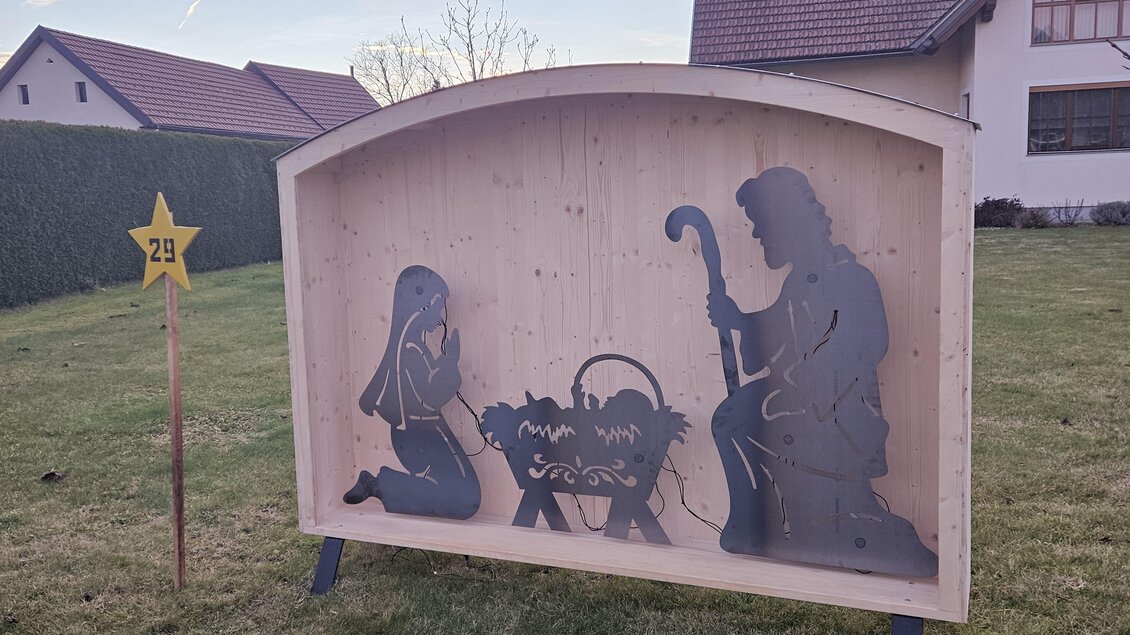 Eine dekorative Holzfigur zeigt eine Krippenszene mit Maria und Josef, die vor dem Jesuskind knien. Im Hintergrund steht ein leuchtender Stern. | © Marktgemeinde Halbenrain