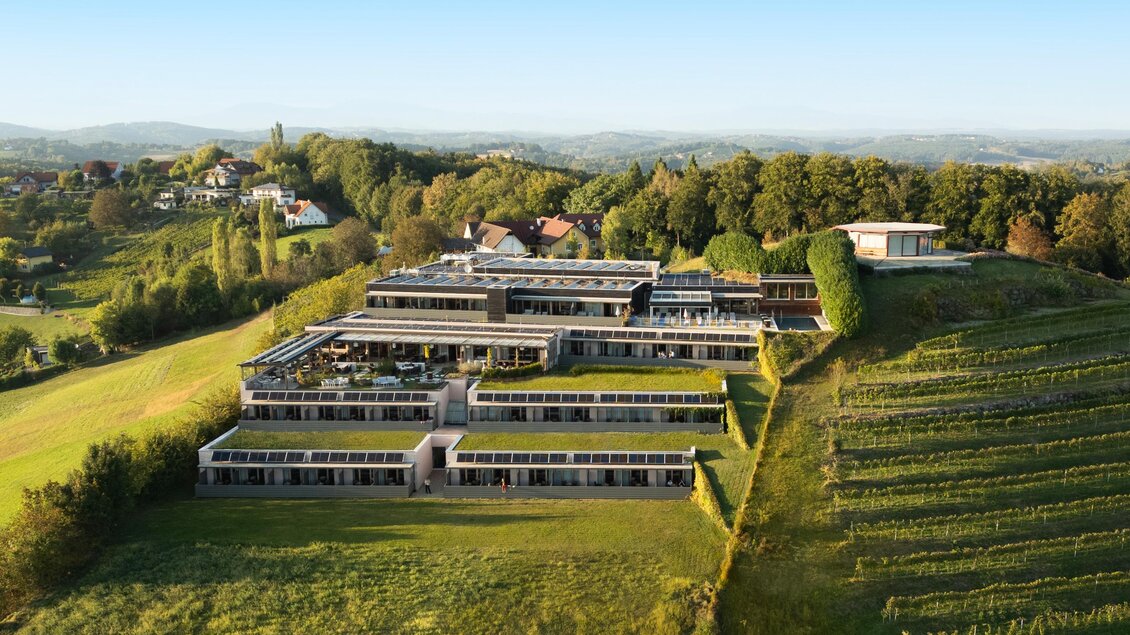 Ein modernes Gebäude inmitten von grünen Weinbergen und Bäumen. Die Architektur fügt sich harmonisch in die Landschaft ein. | © Ingo Pertramer