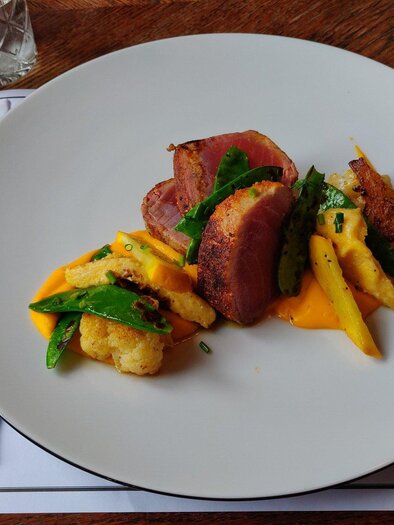 Rosa gebratenes Fleisch mit Gemüse, Kartoffelbeilagen und orangefarbenem Püree, angerichtet auf einem weißen Teller im Kornati. | © Kornati