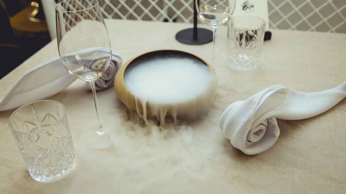 Gedeckter Tisch mit Gläsern und dampfendem Gericht bei Fine Dining in Graz. | © Pixelcoma-Cliff Kapatais