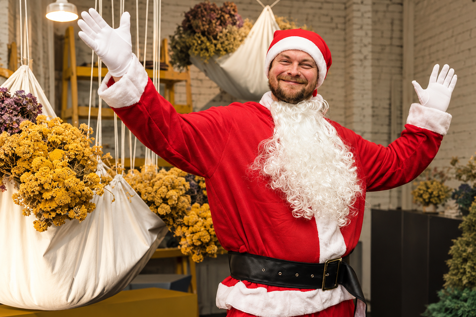 Johann Schmuck im Weihnachtsmannkostüm mit erhobenen Armen, umgeben von hängenden Blumenarrangements im Van den Berg in Graz. | © Nadine Geuter