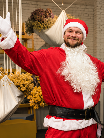 Johann Schmuck im Weihnachtsmannkostüm mit erhobenen Armen, umgeben von hängenden Blumenarrangements im Van den Berg in Graz. | © Nadine Geuter