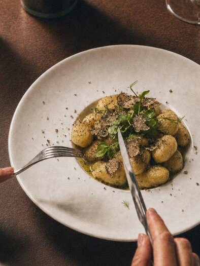 Gnocchi mit gehobeltem Trüffel und frischen Kräutern auf einem weißen Teller, serviert bei Kerzenschein. | © Kornati