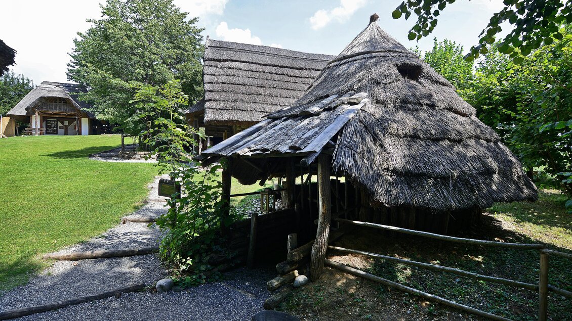 Ein traditionelles, strohgedecktes Haus steht in einer grünen Umgebung. Im Hintergrund sind weitere Gebäude und viel Natur zu sehen. | © Kulmkeltendorf