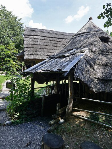A traditional thatched house stands in a green environment. In the background, more buildings and plenty of nature can be seen. | © Kulmkeltendorf