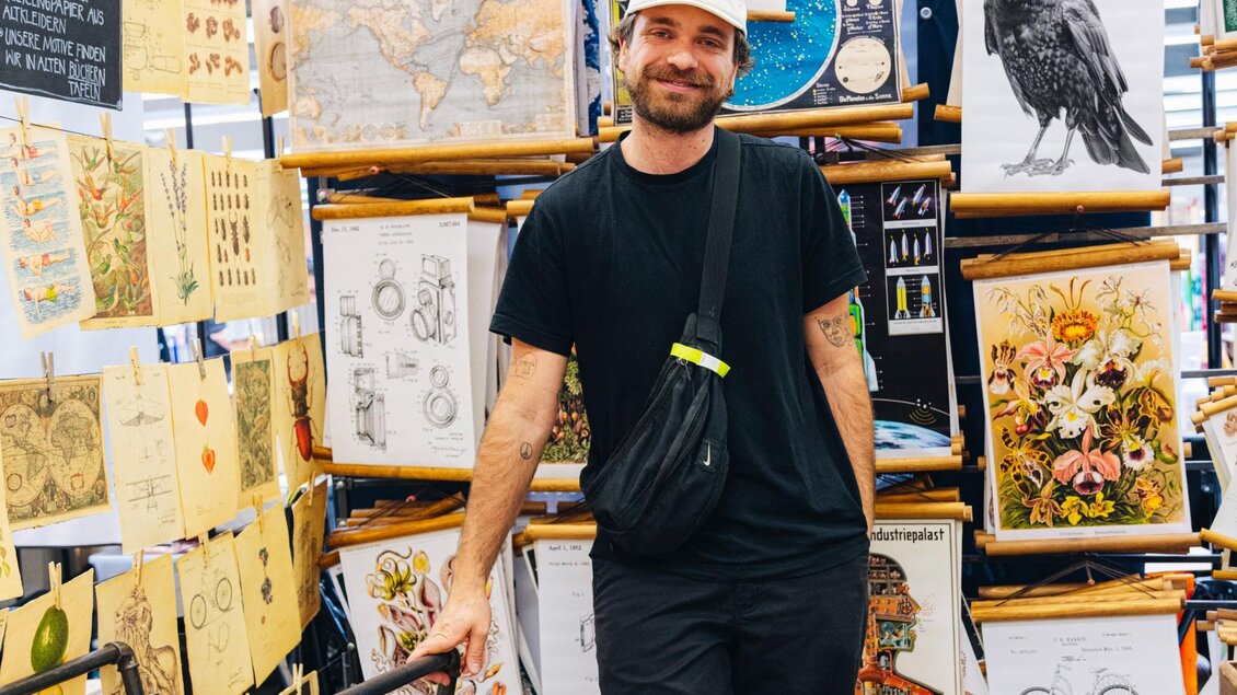 Ein Künstler steht zwischen seinen Illustrationen und Kunstdrucken beim Kunst- und Designmarkt in Graz. | © Franziska Freiwald