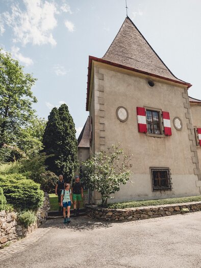 Ein historisches Gebäude mit einem spitzen Dach und roten Fenstern. Der umgebende Garten ist grün und gepflegt. | © TV Hochsteiermark, nicoleseiser.at